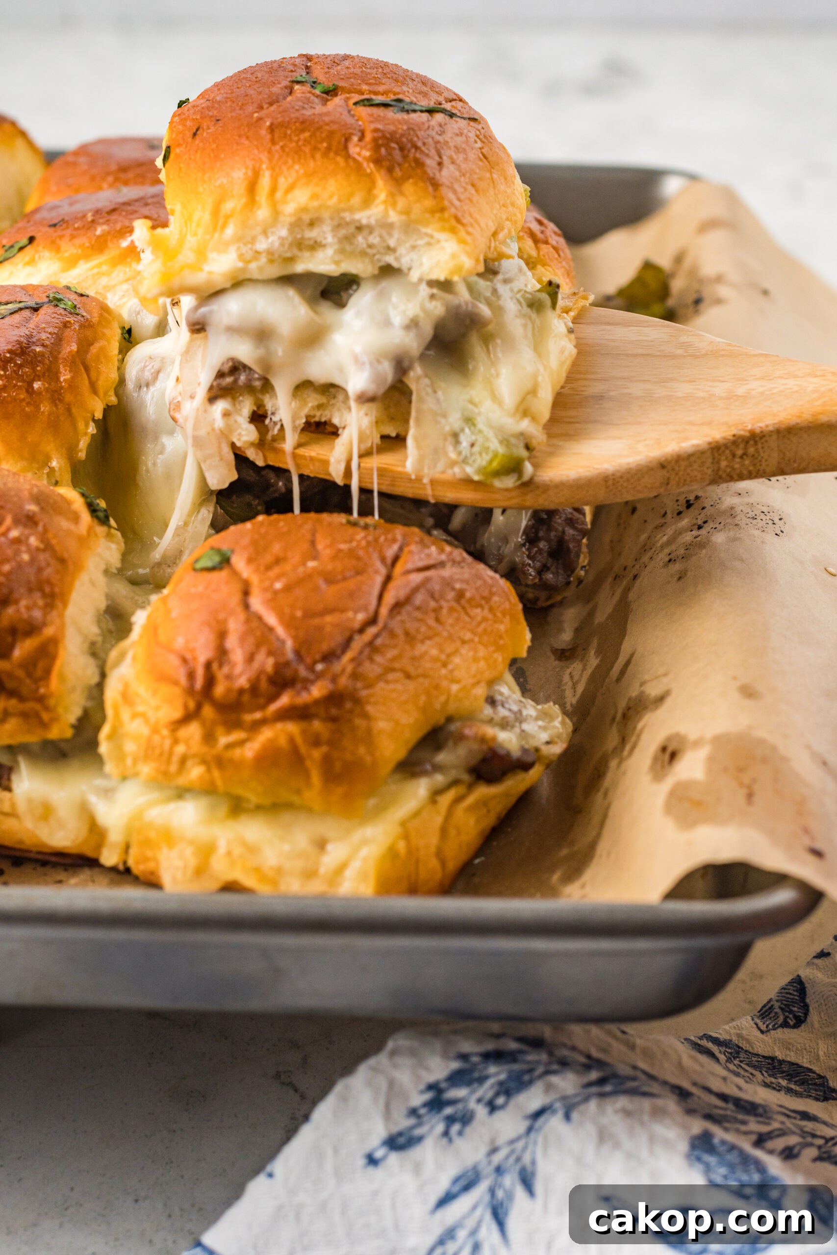 Philly Cheesesteak Sliders Recipe: Savory Mini Sandwiches for Game Day 2 A Philly Cheesesteak Slider being removed from a baking sheet with a wooden spatula.