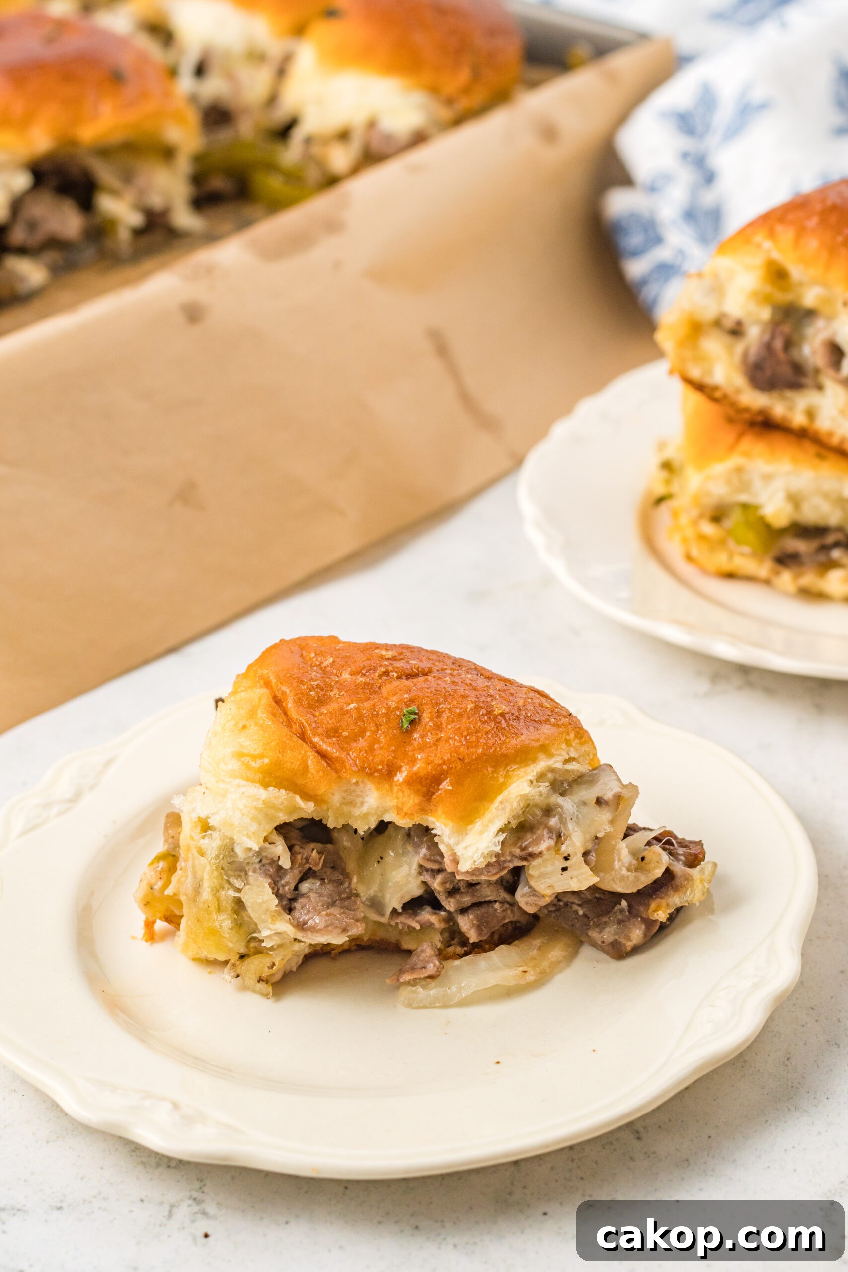 Philly Cheesesteak Sliders Recipe: Savory Mini Sandwiches for Game Day 8 One slider on a white plate with a bite removed showing the cheesy inside.