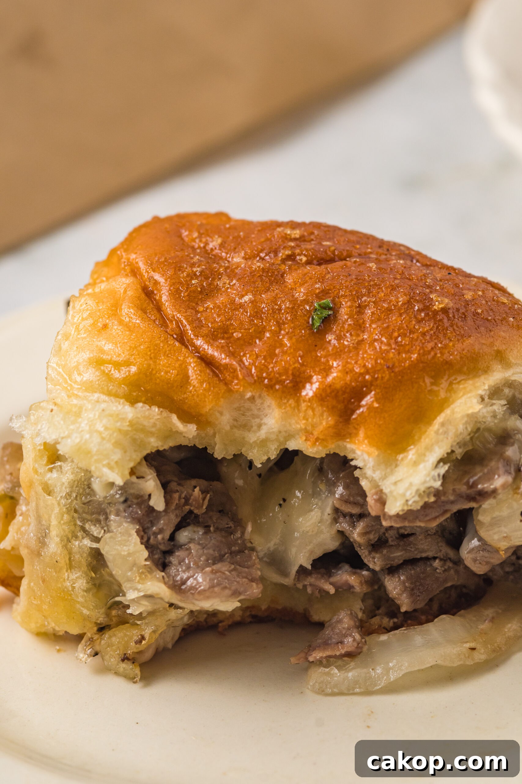 Philly Cheesesteak Sliders Recipe: Savory Mini Sandwiches for Game Day 10 One slider on a white plate with a bite removed showing the inside.