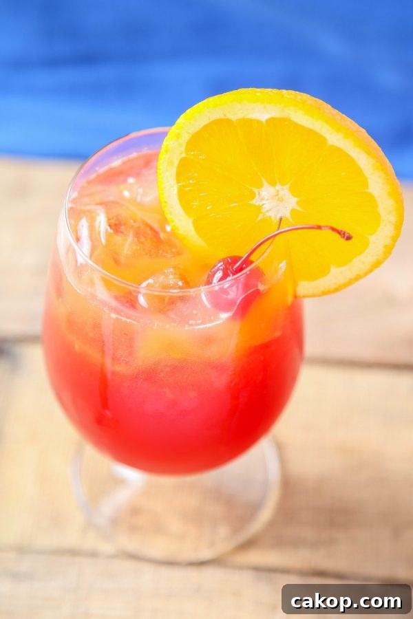 a hurricane drink in a hurricane glass with an orange slice and cherry garnish.