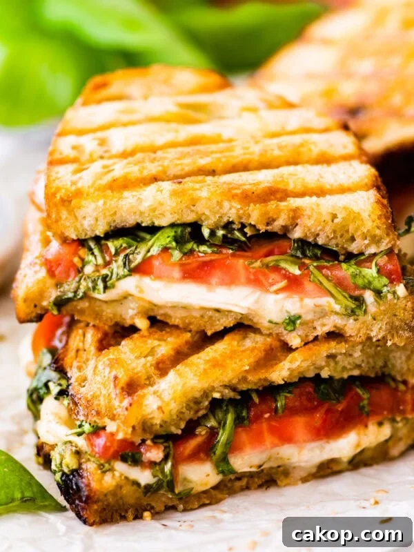 Stack of two halves of Caprese sandwich with basil pesto on parchment paper.