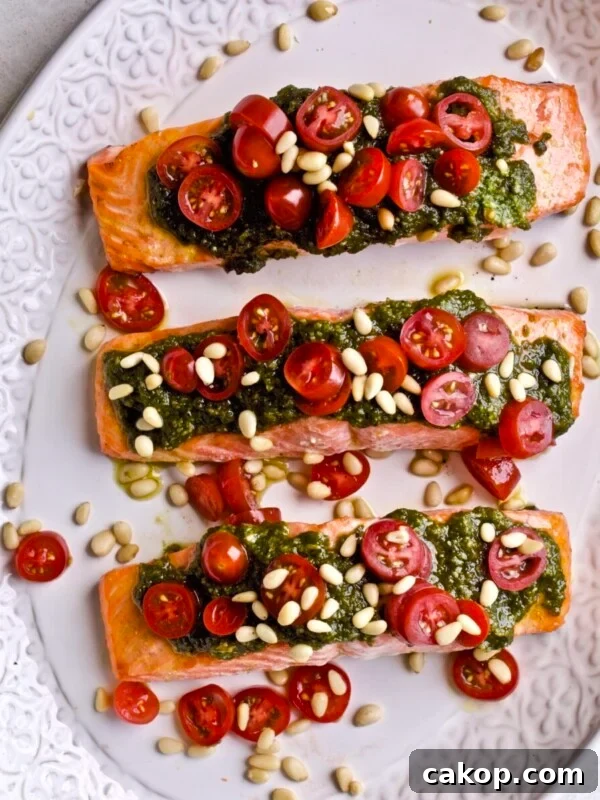 beautifully plated salmon. Three fillet on a platter with pestoover the top, cheery tomatoes, and pine nuts!