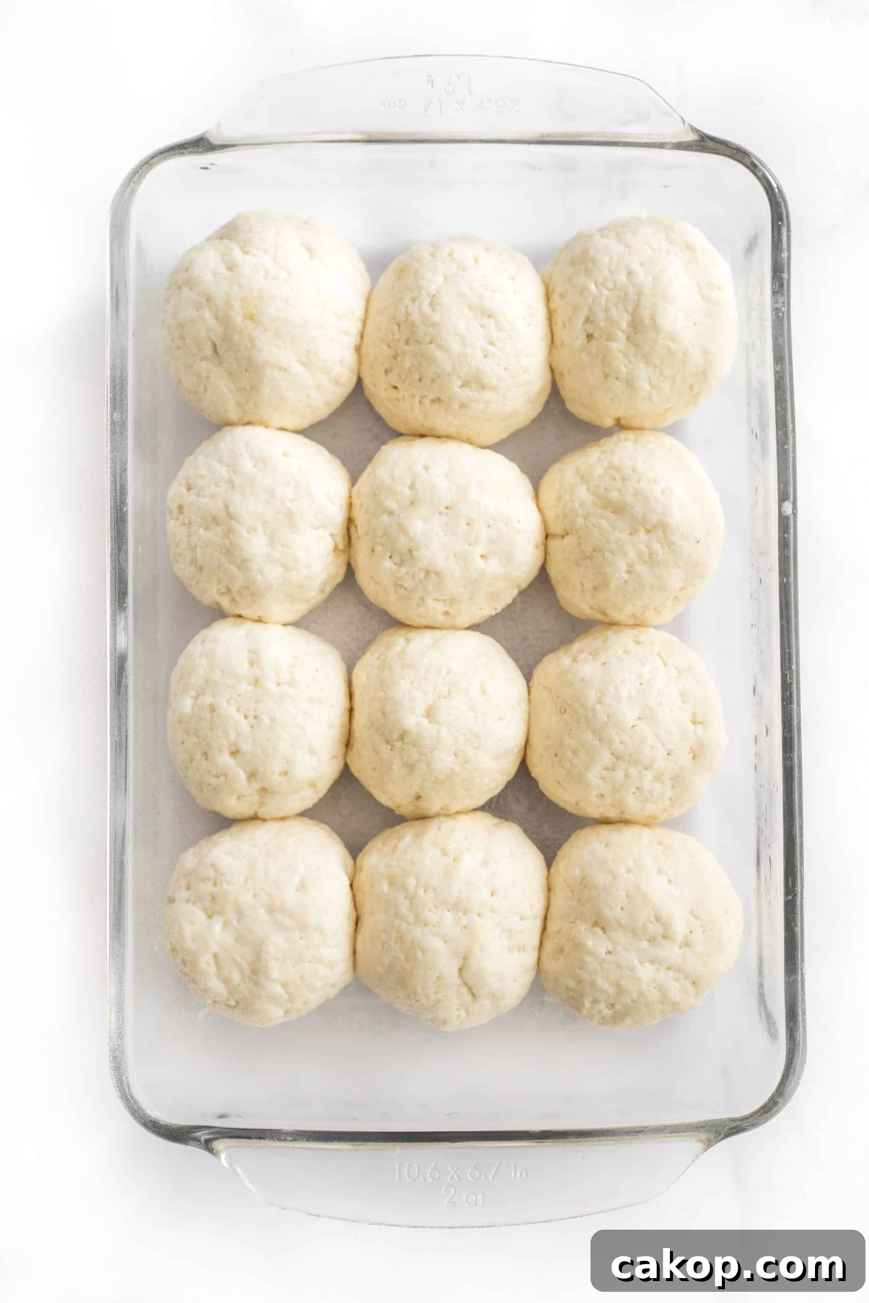 Gluten-Free Soft Dinner Rolls (Dairy-Free) Balls of bread dough rising in a glass pan.