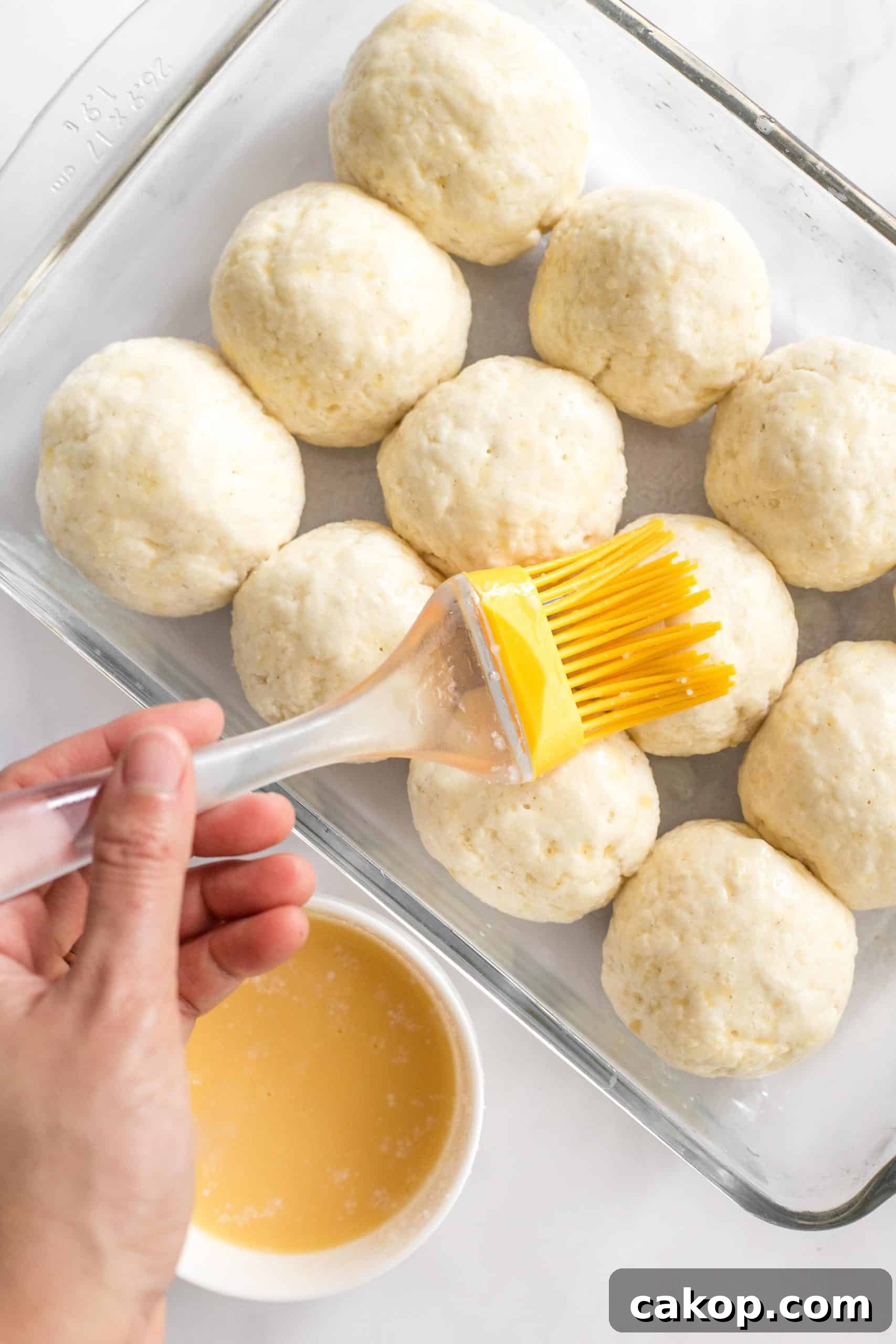Soft Gluten-Free Dairy-Free Dinner Rolls Hand brushing unbaked bread rolls with egg wash.
