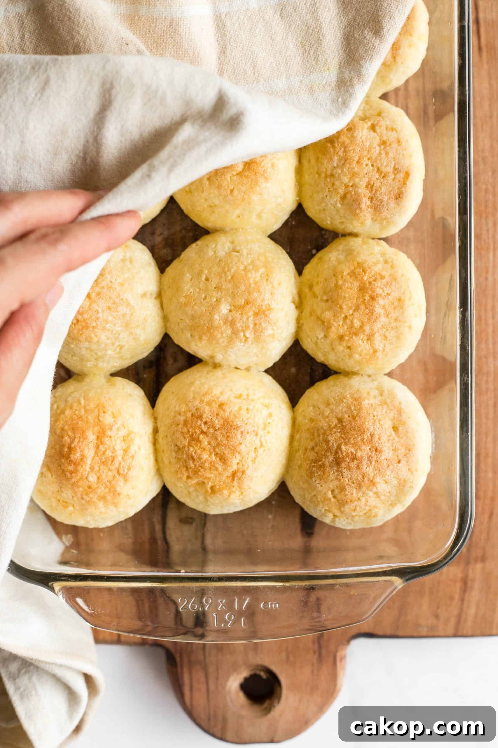 Soft Gluten-Free Rolls (Dairy-Free) Removing a kitchen towel covering a glass pan full of gf dinner rolls.