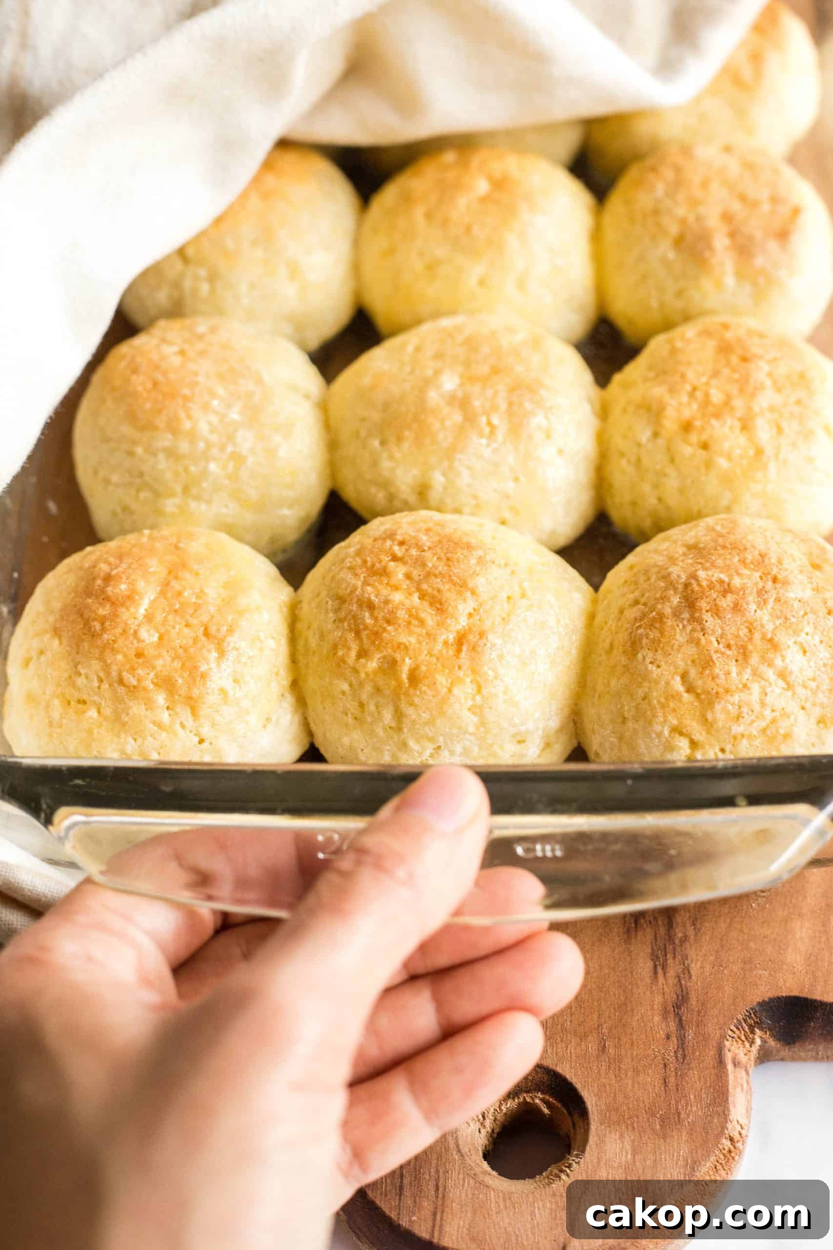 Soft Gluten-Free Yeast Rolls (Dairy-Free) Hand holding a glass pan full of gluten-free bread rolls.