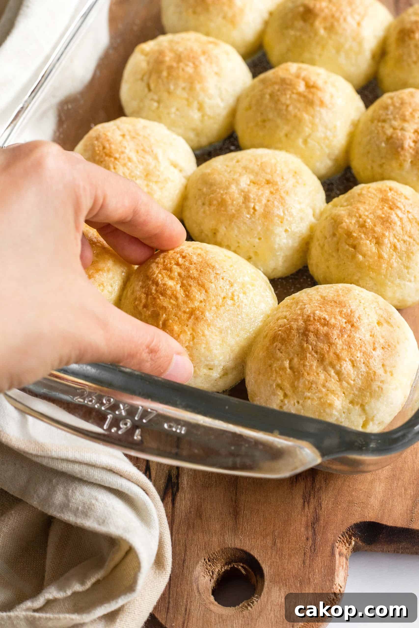 Soft Gluten-Free Bread Rolls (Dairy-Free) Hand reaching for gluten-free bread rolls in a glass baking pan.