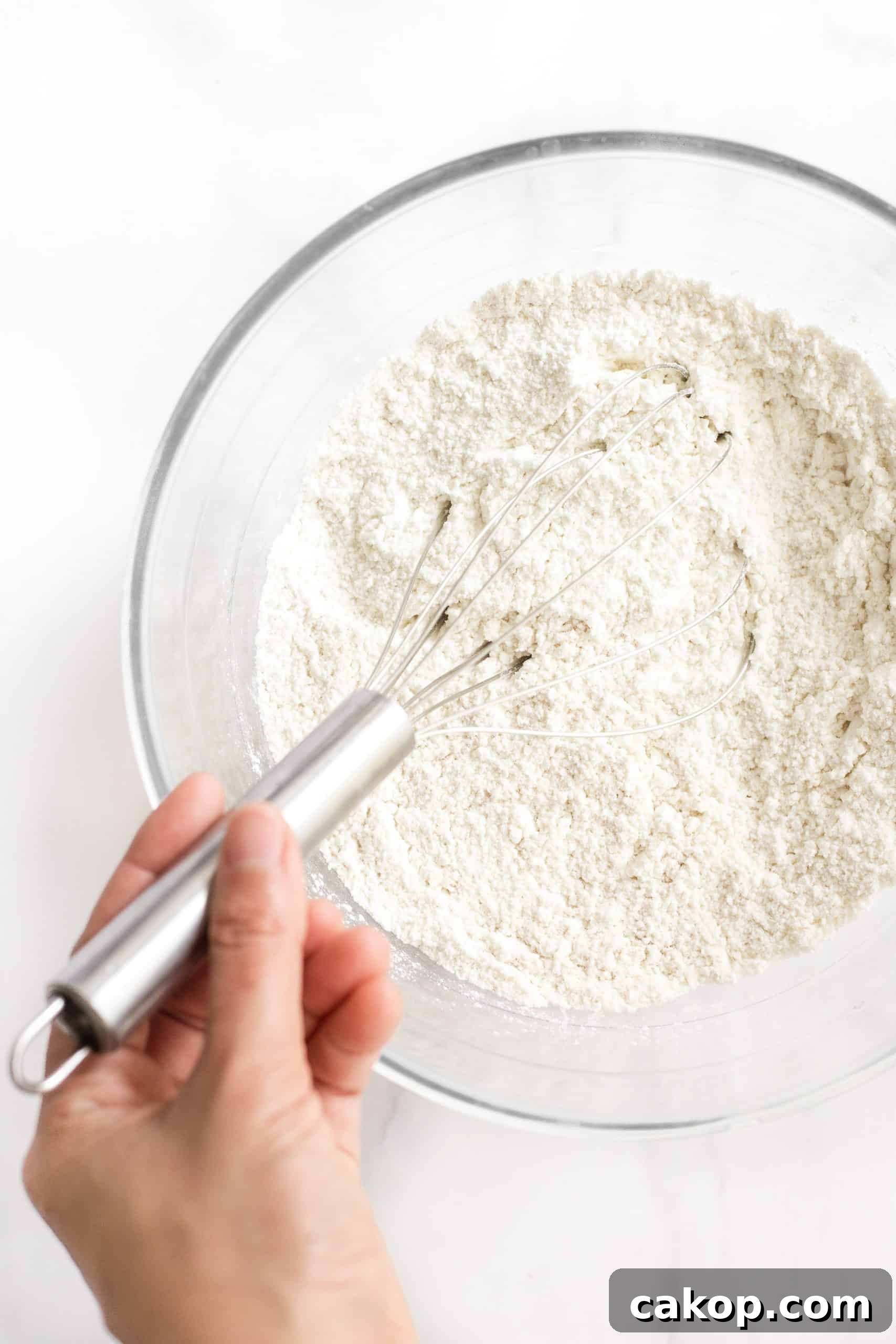 Soft Dinner Rolls (Gluten-Free, Dairy-Free) Hand whisking dry ingredients in a glass mixing bowl.