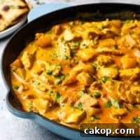 A cast iron pan full of chicken and potato curry garnished with cilantro, with a plate of naan bread in the background.