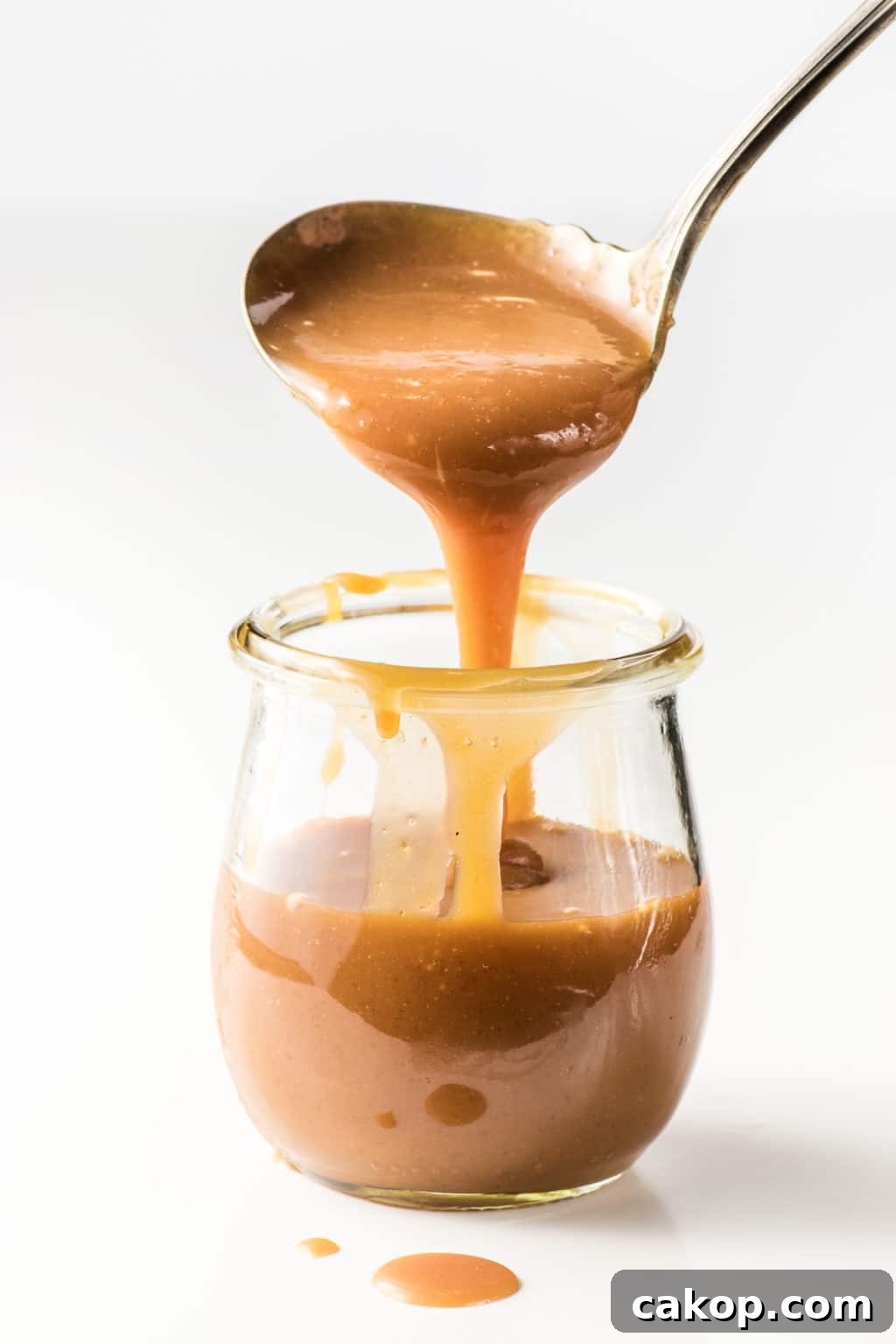 A small jar of keto caramel sauce. Caramel is being scooped out with a mini ladle.