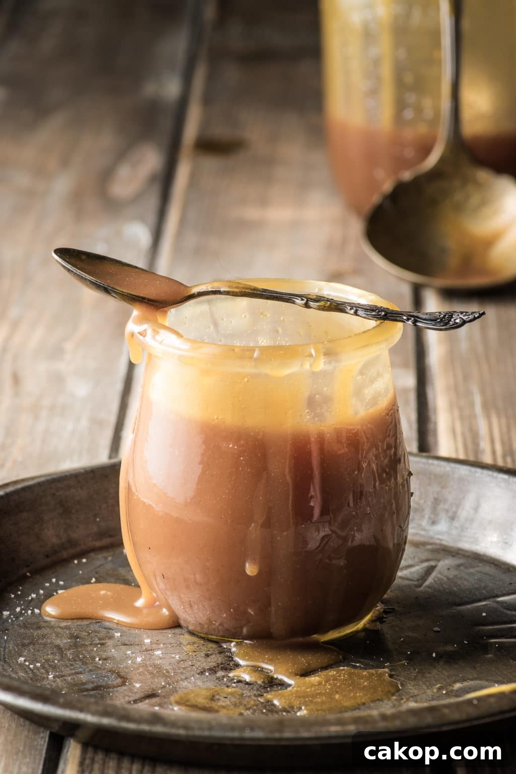 A jar of keto caramel sauce, with sauce dripping down the sides and pooling on the table.