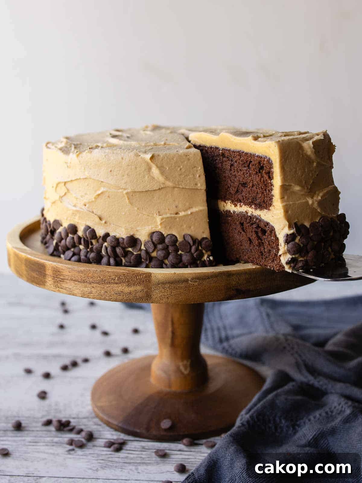Decadent Chocolate Peanut Butter Cake Recipe 2 Chocolate and peanut butter cake on a wooden cake stand with a slice cut.
