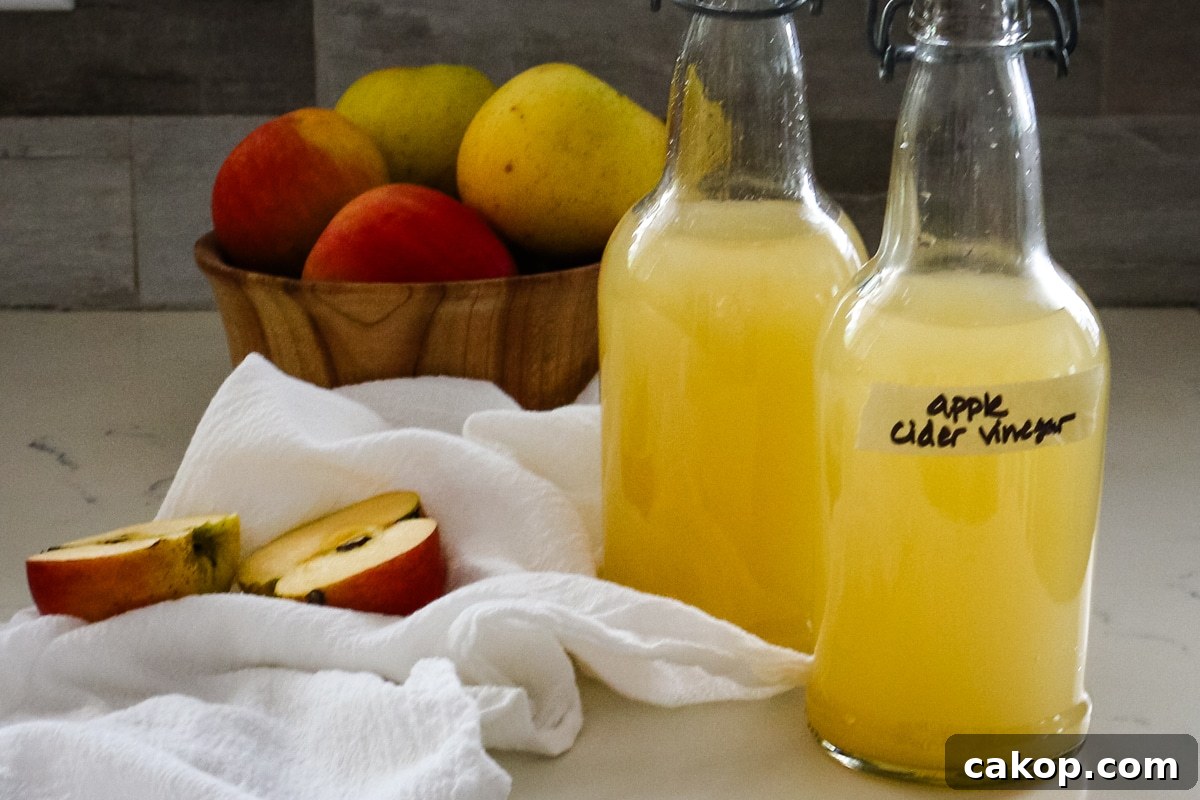 two swing-top bottles of homemade apple cider vinegar next to a bowl of fresh apples.