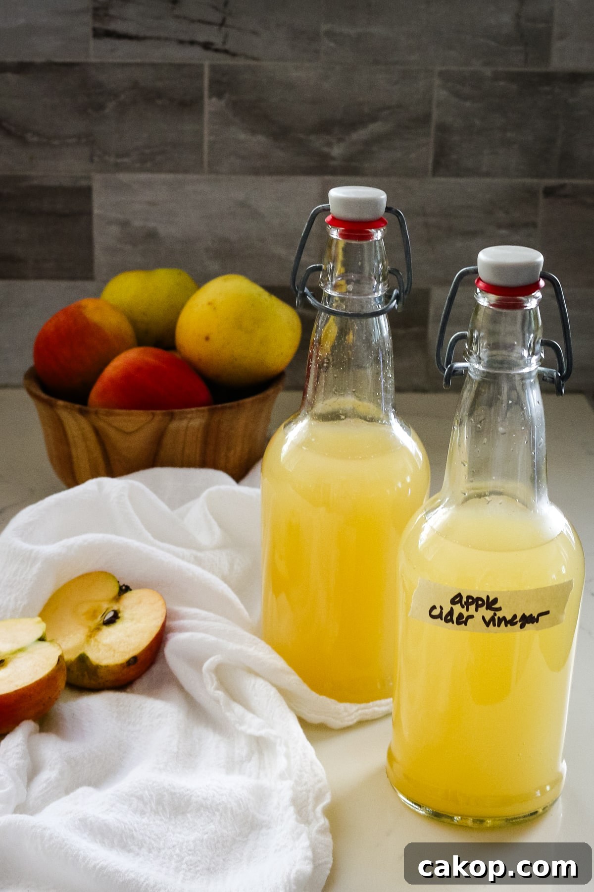 two swing-top bottles of homemade apple cider vinegar next to a bowl of fresh apples.