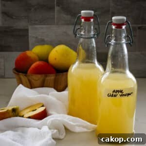 two swing-top bottles of homemade apple cider vinegar next to a bowl of fresh apples.