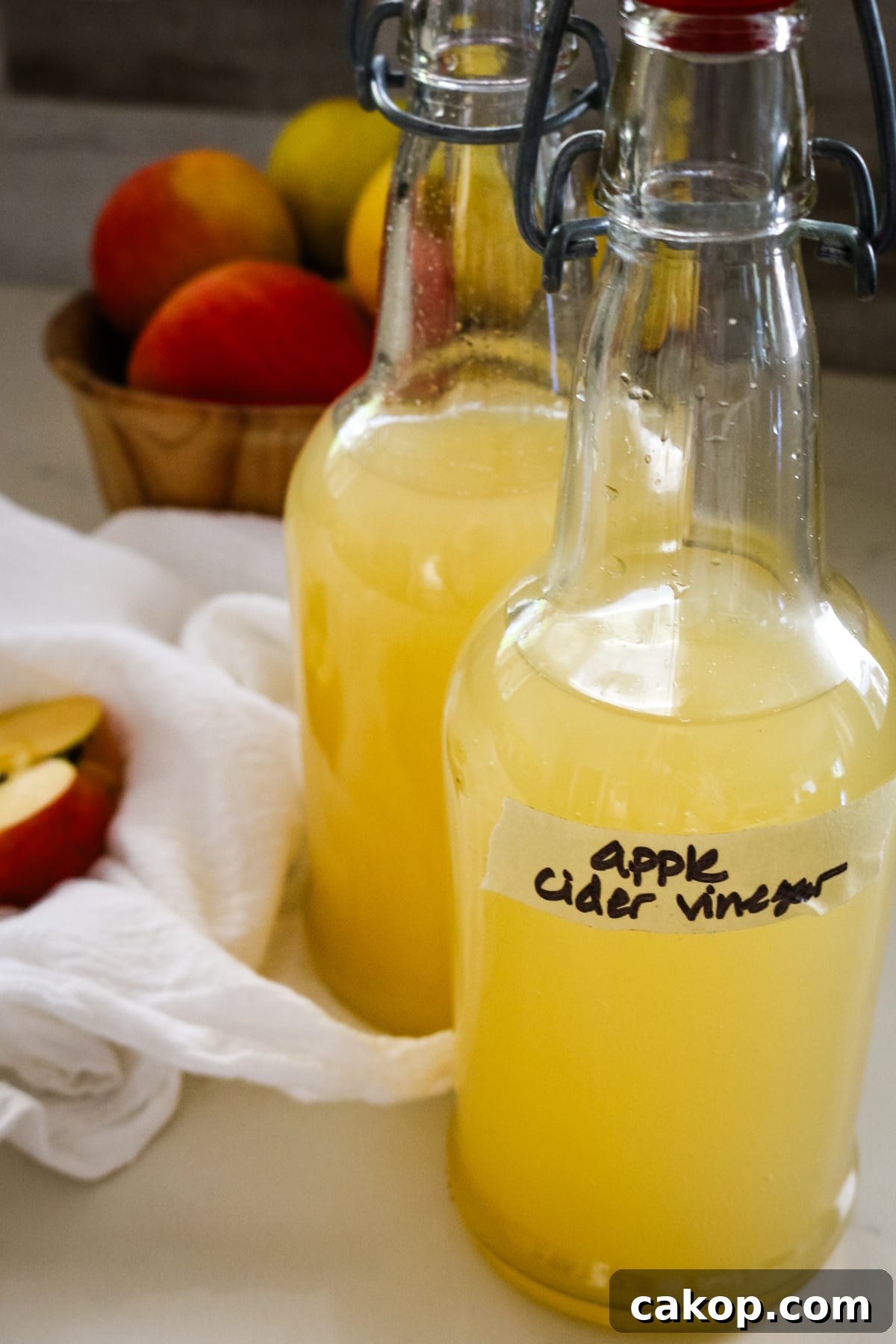 two swing-top bottles of homemade apple cider vinegar next to a bowl of fresh apples.