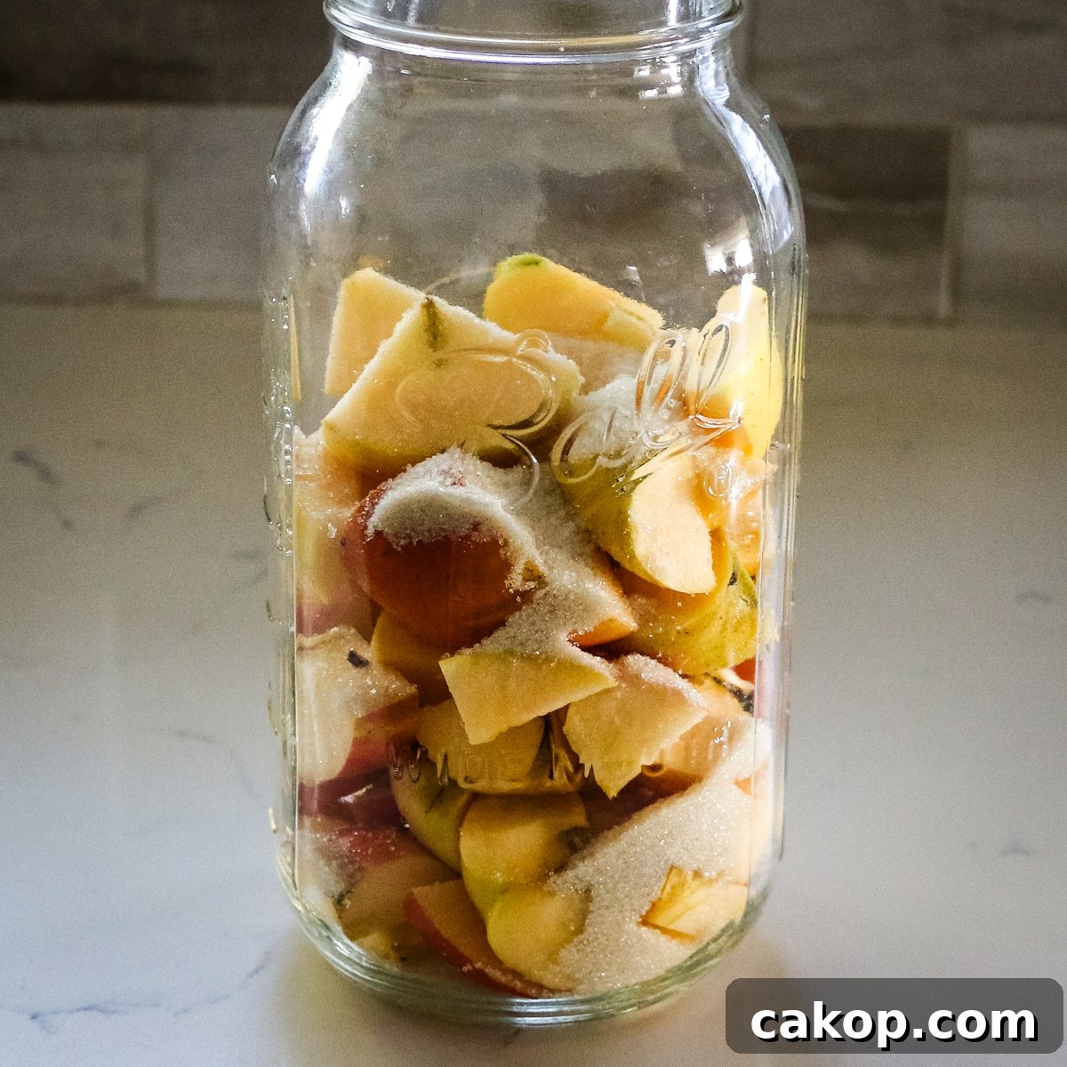 chopped apple scraps sprinkled with sugar inside a clear mason jar, ready for fermentation.