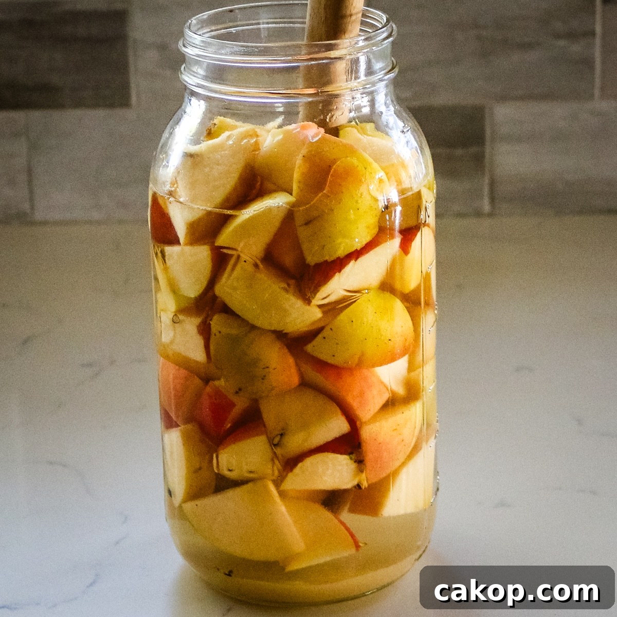 large glass jar filled with chopped apples and liquid for fermentation.