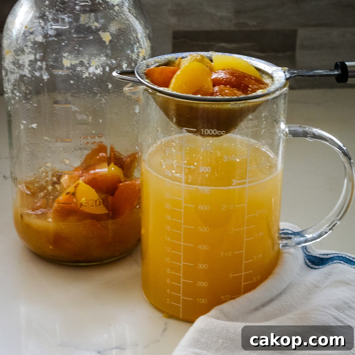 large glass jar and measuring cup showing the process of straining fermented apple solids from the liquid.
