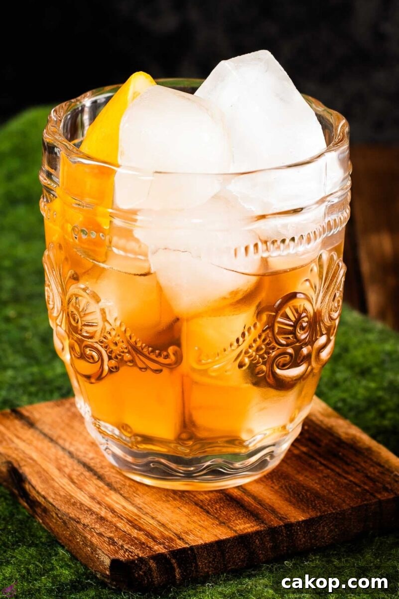 Gorgeous glass filled with maple old fashioned on wooden coaster. The drink is garnished with an orange zest.