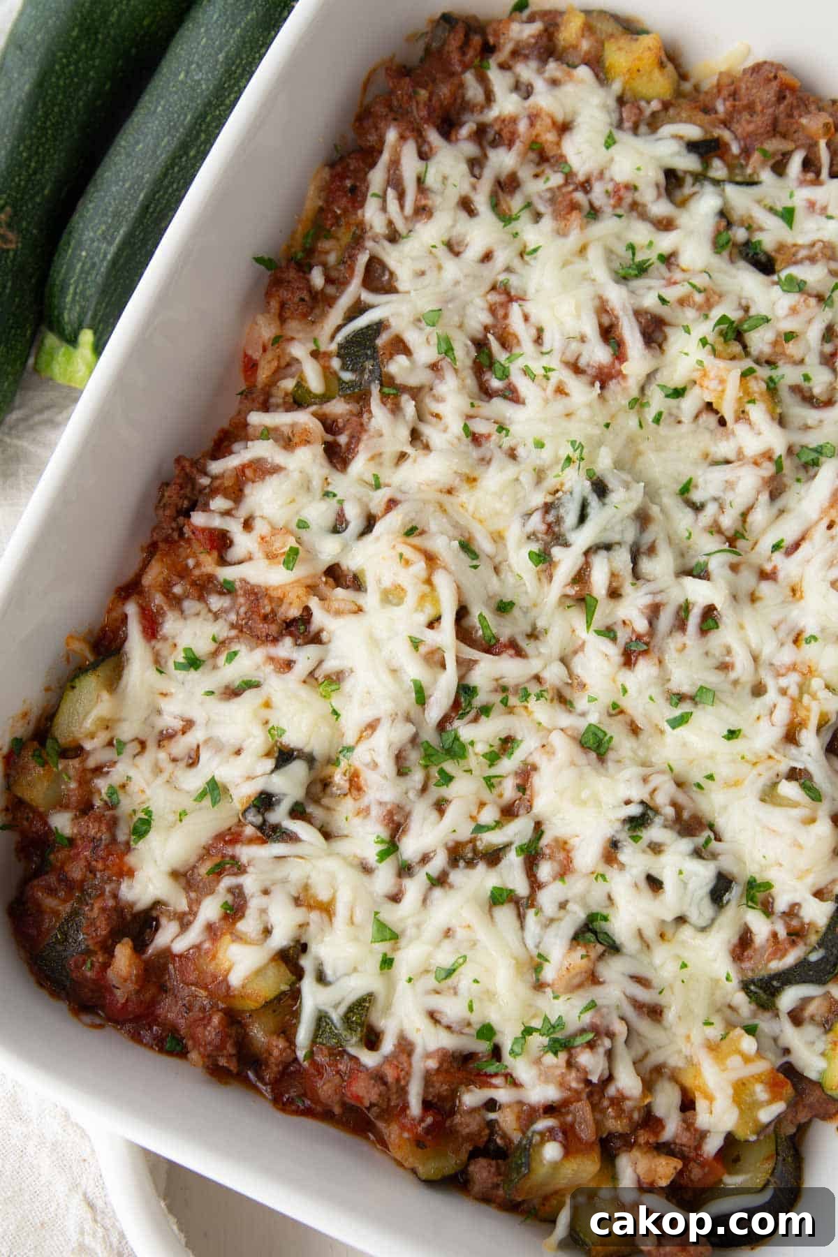 zucchini, ground beef, and tomatoes in a casserole dish topped with shredded cheese.