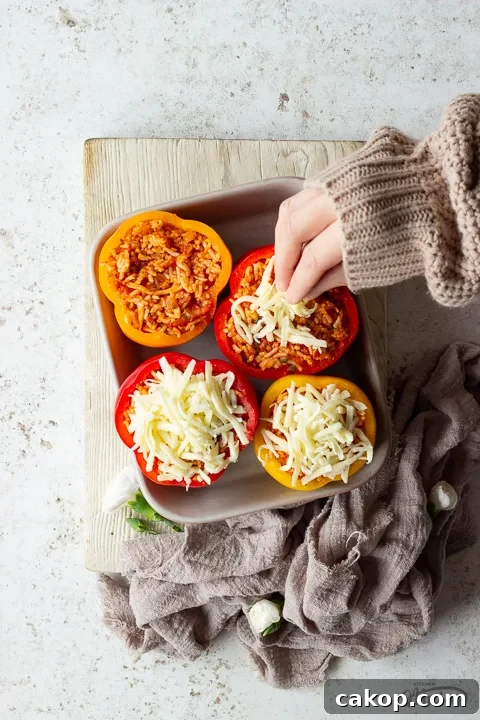 Someone topping rice stuffed peppers with grated mozzarella