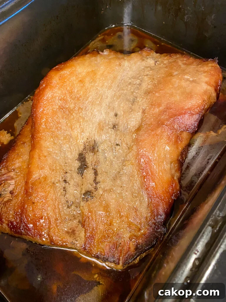 Layer of golden brown fat on top of cooked brisket in beef juices and marinade in a roaster oven