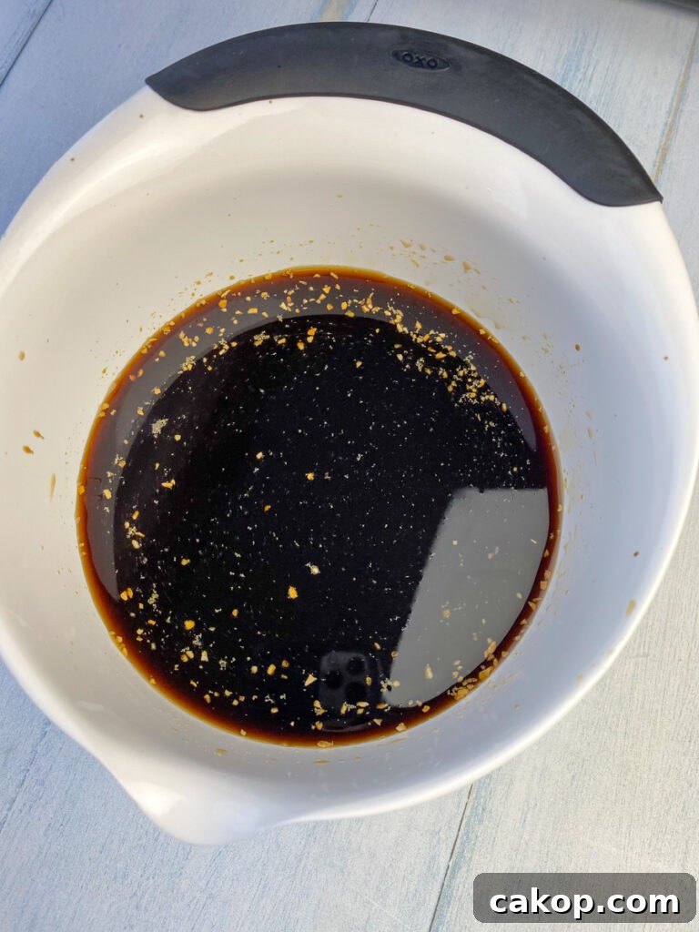 Soy sauce, beef consomme and garlic in a marinade in white bowl