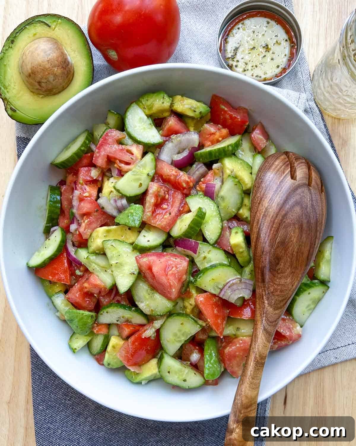 Creamy Avocado and Tomato Salad with Lime and Basil 2 white dish with salad and wooden spoon in salad on the right side.