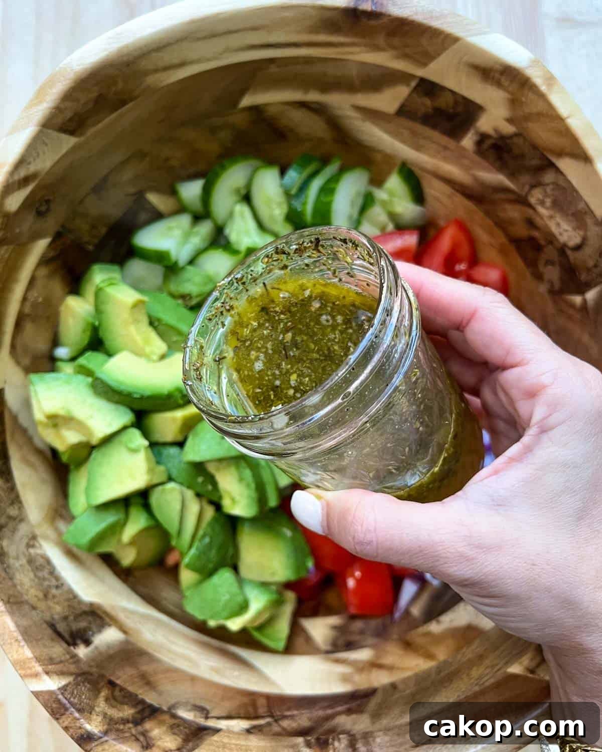 Creamy Avocado and Tomato Salad with Lime and Basil 7 Hand-holding mason jar with salad dressing, pouring it.