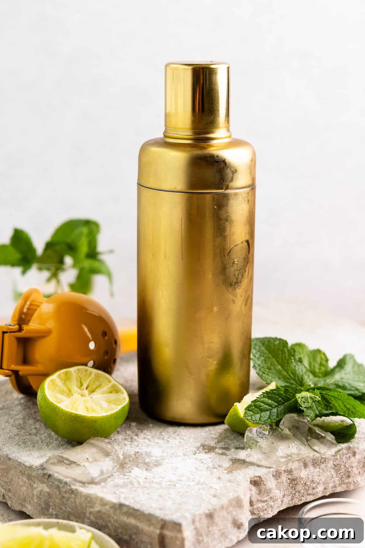 Gold cocktail shake surrounded by mint leaves and lime.