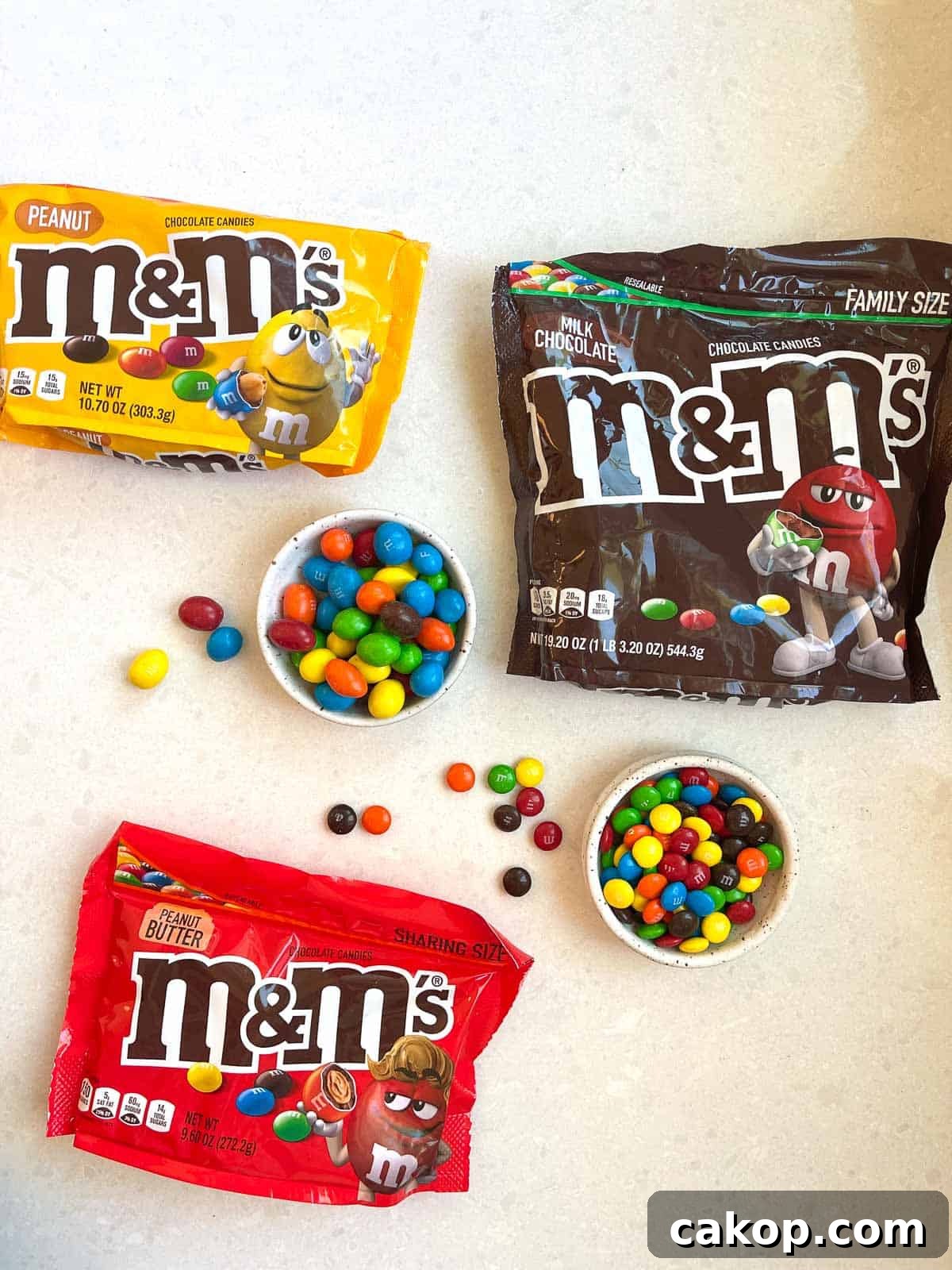 3 bags of M&Ms on white counter with 2 bowls of open mms