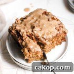 A square slice of apple coffee cake with maple glaze on a small white plate with a fork. A square slice of apple coffee cake with maple glaze on a small white plate with a fork.