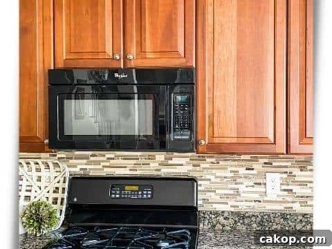 Cherry kitchen with a glass tile backsplash and busy granite counter and black appliances during a renovation