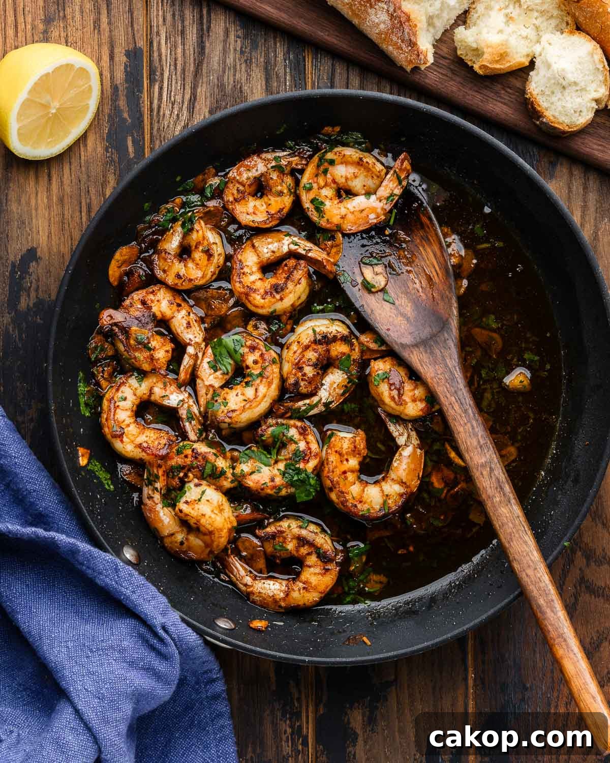 Spanish garlic shrimp in black pan with wooden spoon along with lemon and crusty bread on the side.