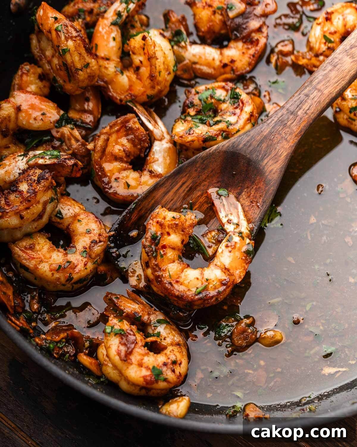 Gambas al ajillo in black pan with wooden spoon holding a shrimp.