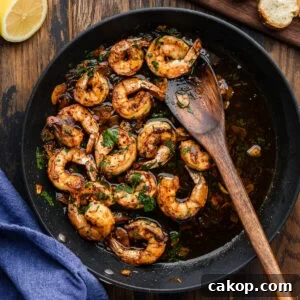 Gambas al ajillo in black pan with wooden spoon.