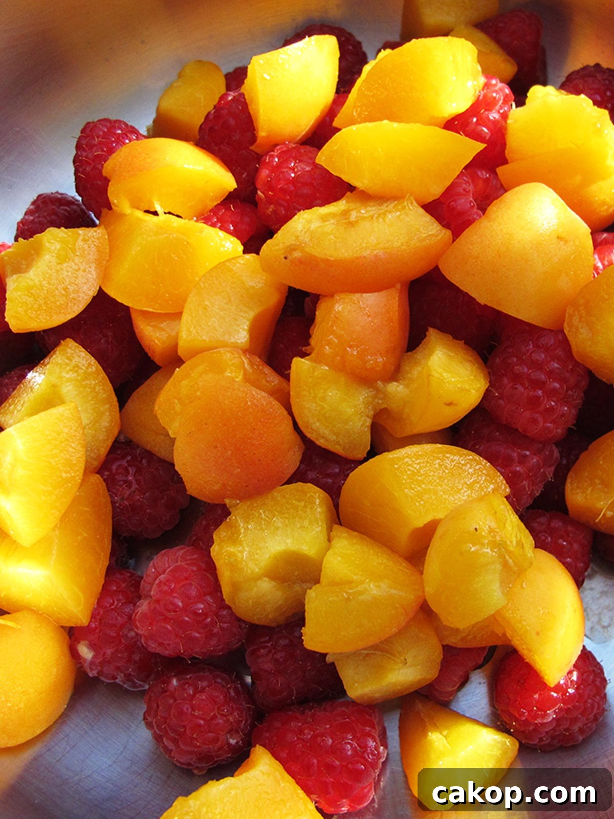 Chopped apricots and raspberries in pot with lemon juice ready to cook.