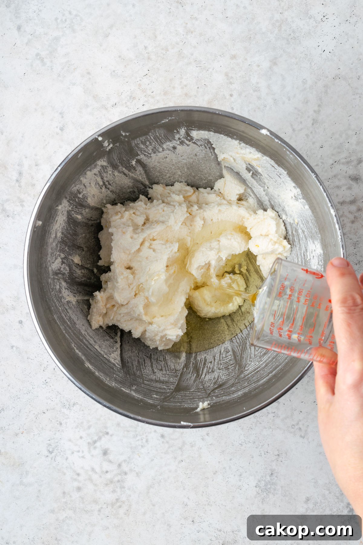 Oil being poured into the bowl with the creamed butter and sugar.