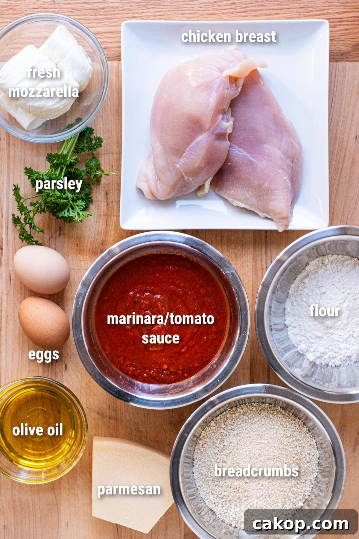 Raw, uncooked chicken parmesan ingredients laid out on a wooden cutting board.