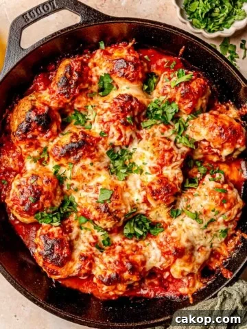 Meatballs in a cast iron skillet topped with mozzarella cheese and parsley.