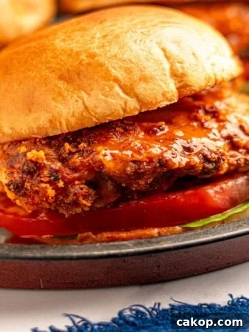 Close up view of a crispy buffalo chicken sandwich on a bun with lettuce and tomato.