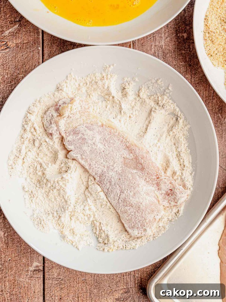 A piece of chicken in a bowl of flour.