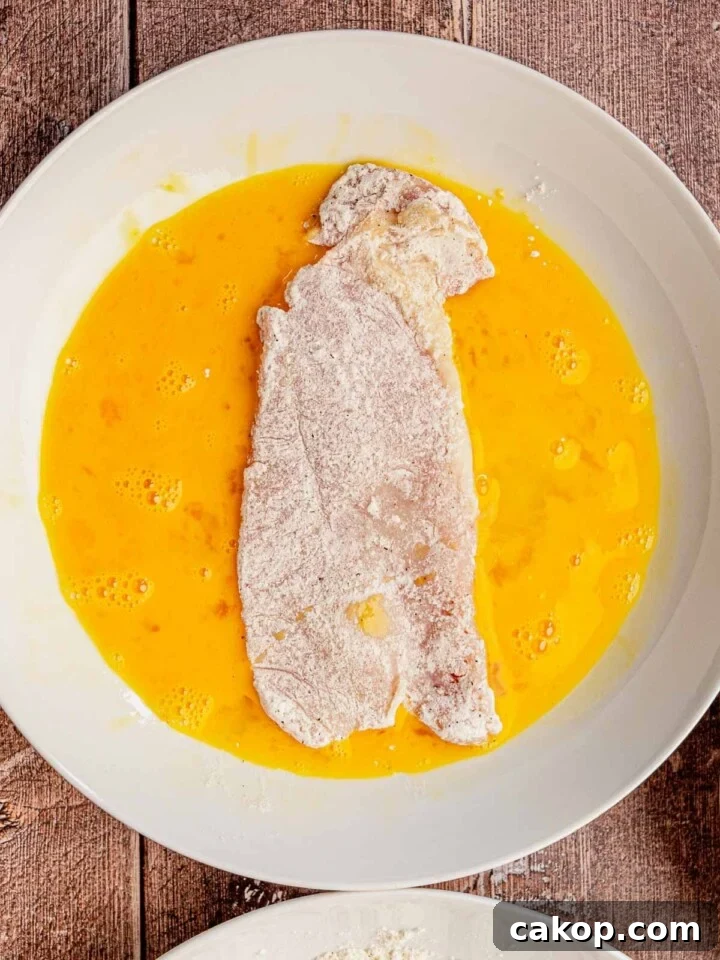 A piece of chicken in a bowl of egg wash.