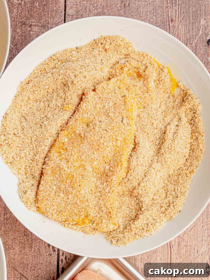 A piece of chicken in a bowl of breadcrumbs.