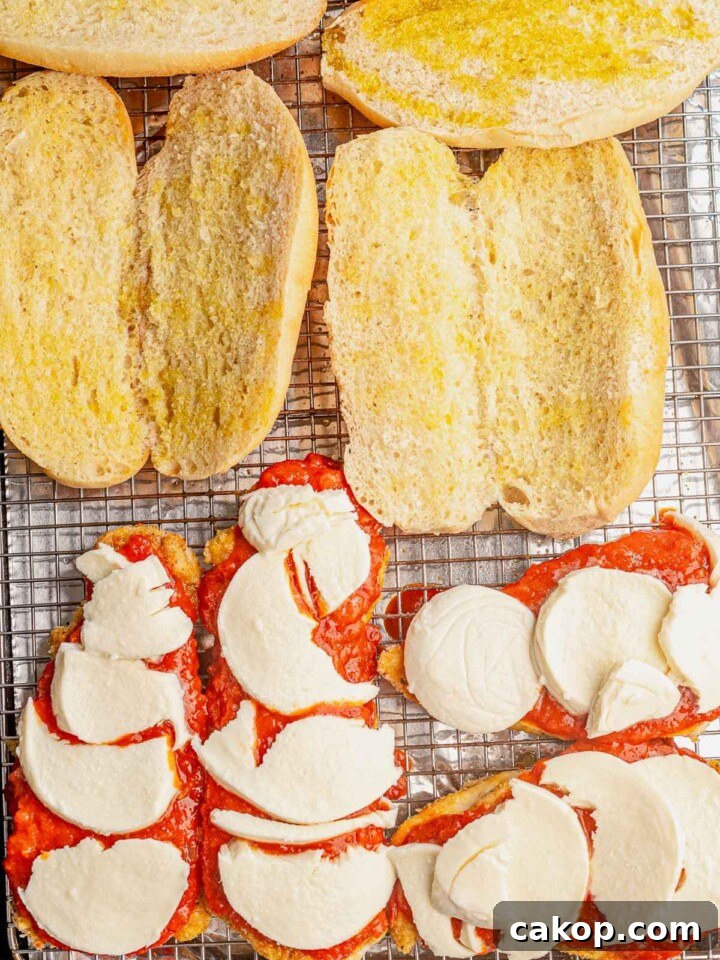 Sub rolls and chicken topped with mozzarella on a sheet pan.