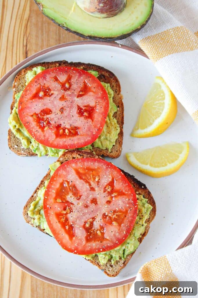 Creamy Avocado Toast with Fresh Tomato and Basil 2 Two slices of avocado toast with tomato on a white plate garnished with lemon slices.