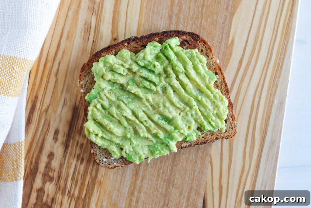 Creamy Avocado Toast with Fresh Tomato and Basil 5 A slice of whole grain bread topped with mashed avocado on a wooden board.