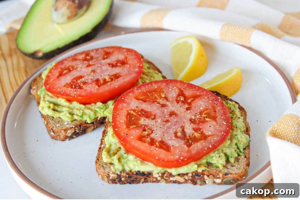 Creamy Avocado Toast with Fresh Tomato and Basil 6 Two slices of avocado toast with tomato on a white plate garnished with lemon slices.
