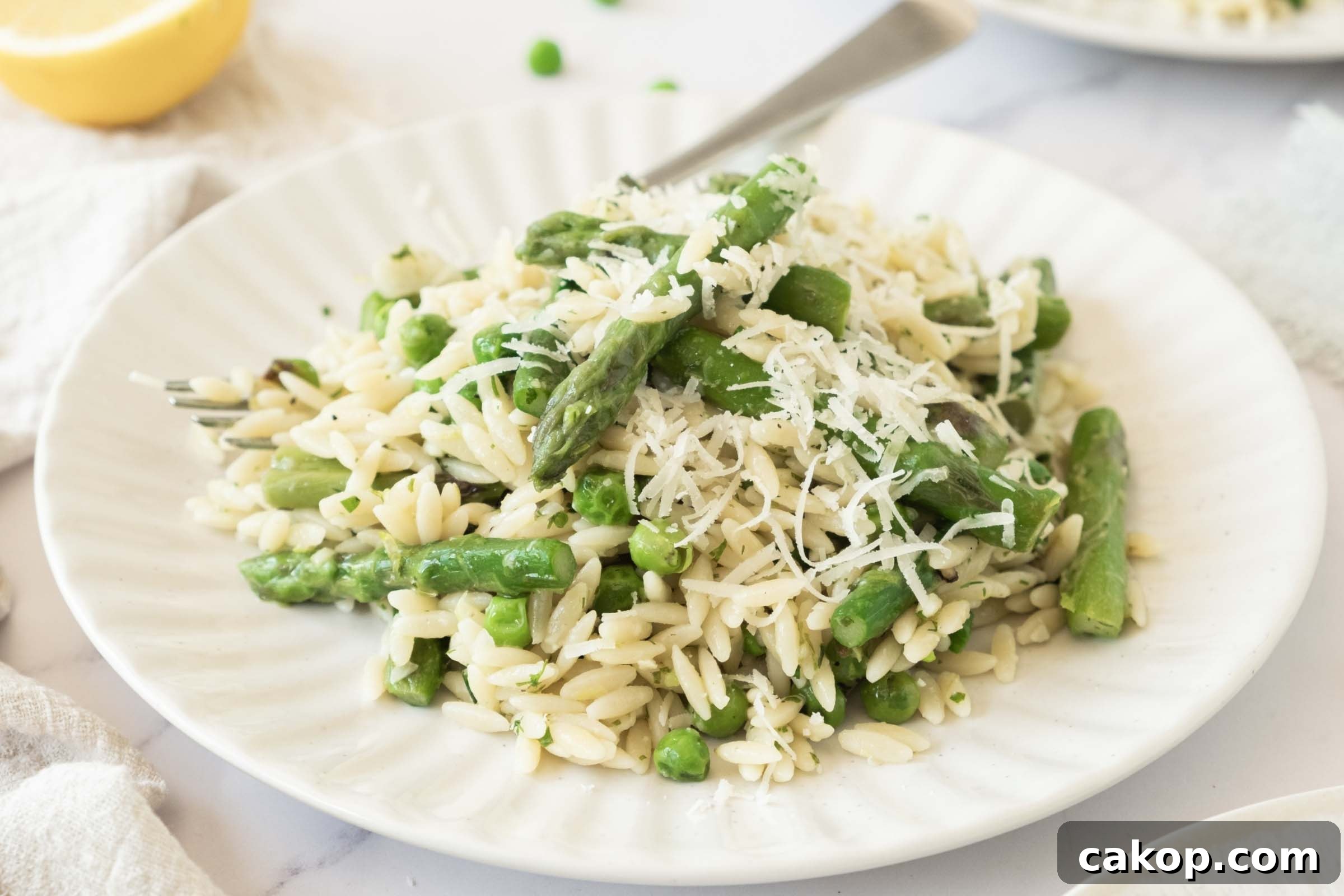 Plate of orzo with peas and asparagus garnished with grated Parmesan cheese.